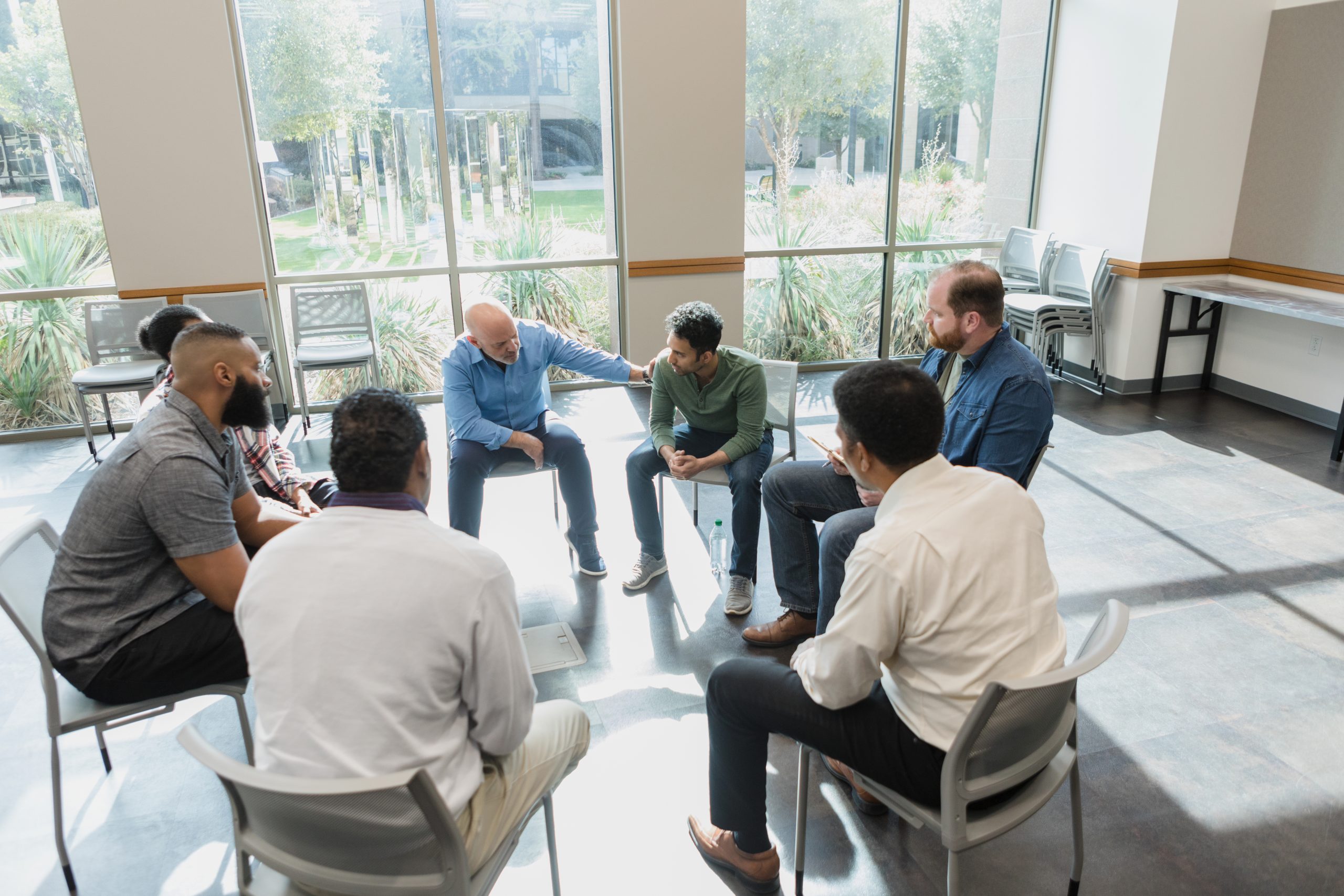 The diverse group of men sit in a circle and talk about grief during their group therapy session at the community center.