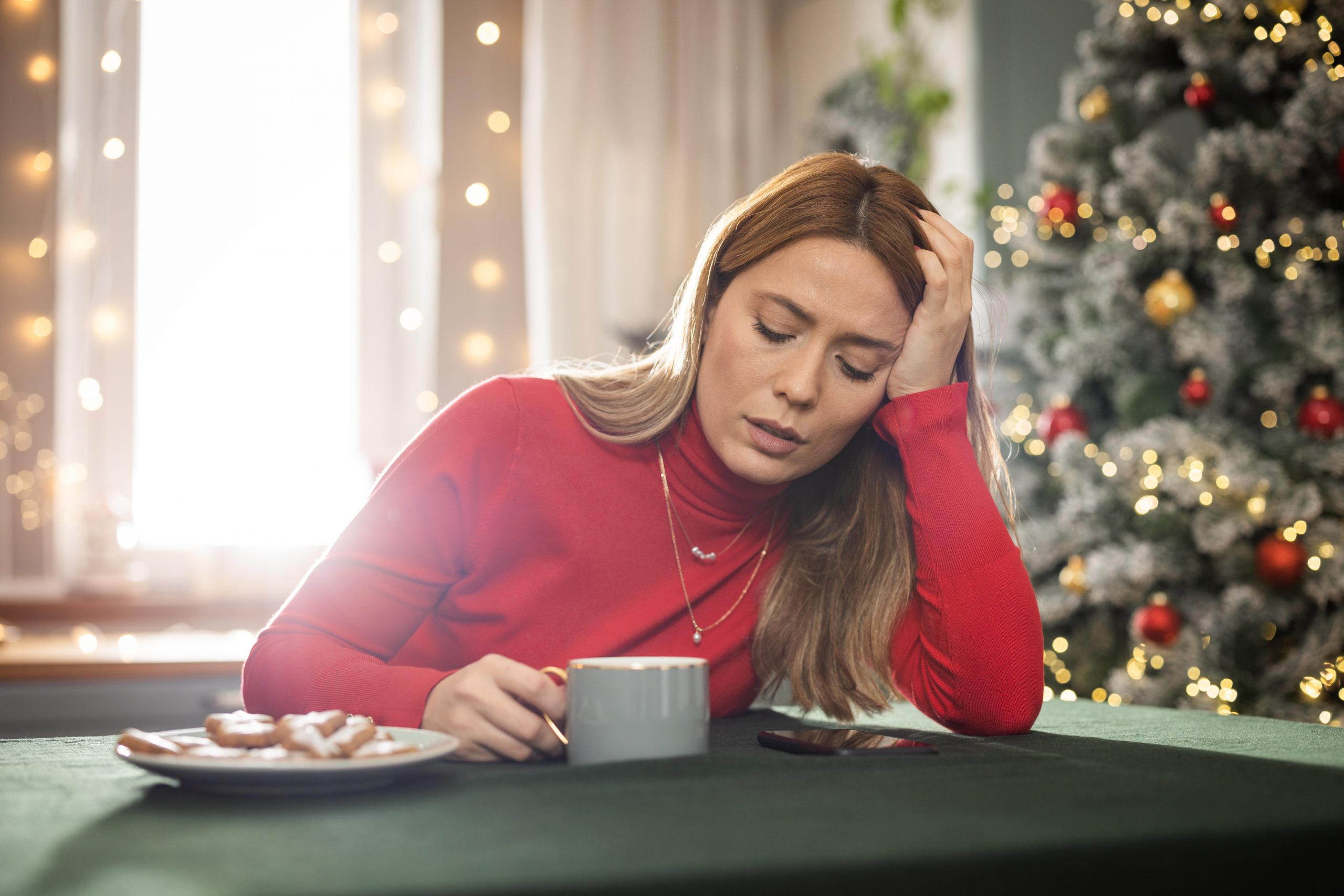Young sad woman sitting near the Christmas tree in kitchen