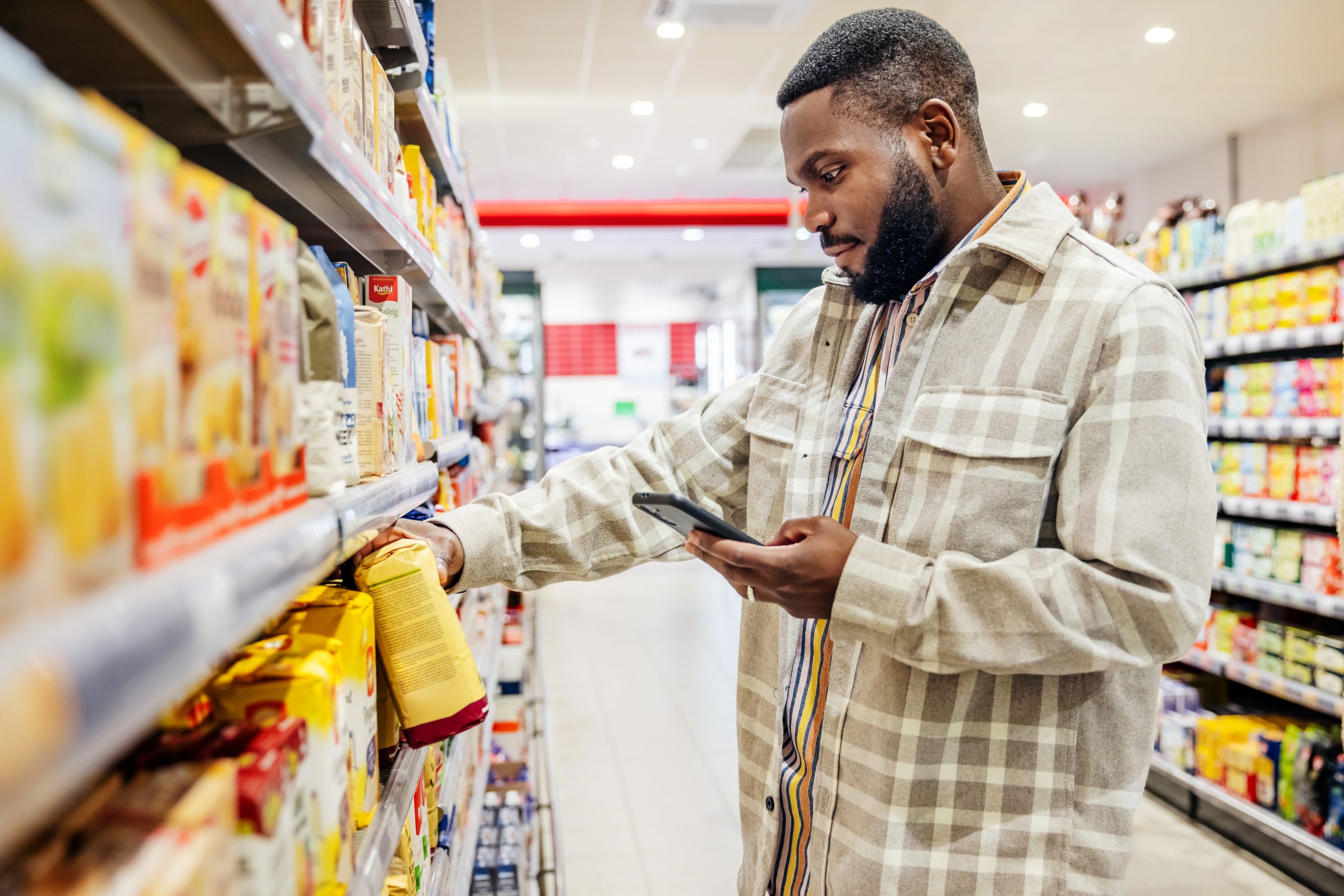 A man using his smartphone to look up ingredients and prices wile choosing items in his local supermarket.