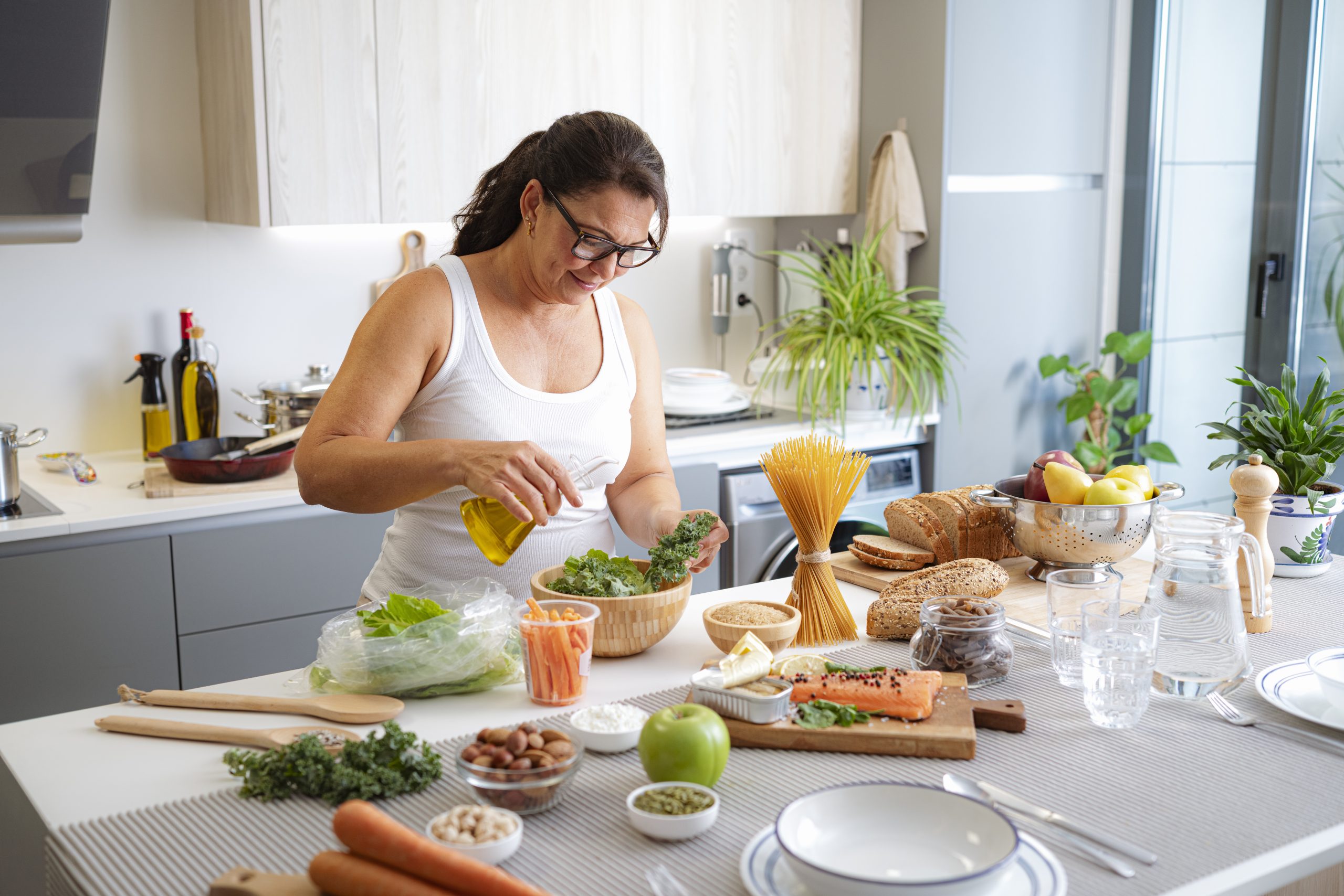 Woman, salad bowl and healthy food. Person in the kitchen preparing a well balanced meal. Olive oil, fruits, vegetables and salmon. Diet to control the obesity and boost metabolism Woman, salad bowl and healthy food. Person in the kitchen preparing a well balanced meal. Olive oil, fruits, vegetables and salmon. Diet to control the obesity and boost metabolism