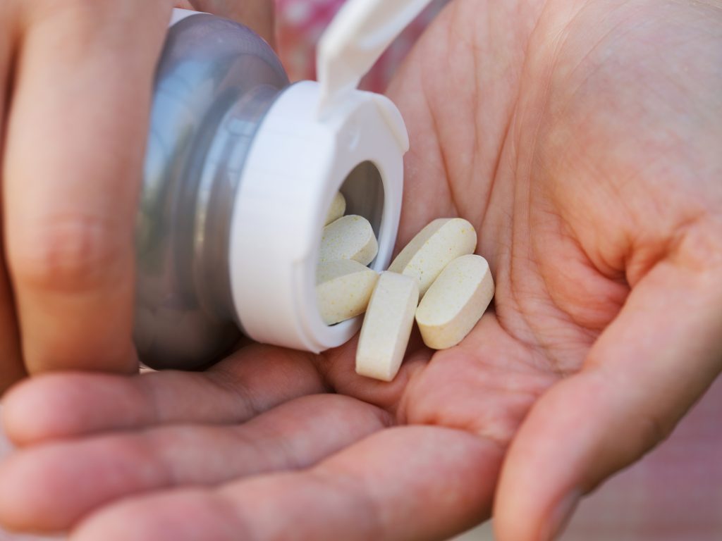 A woman pouring magnesium taurate tablets out of a bottle into the palm of her hand