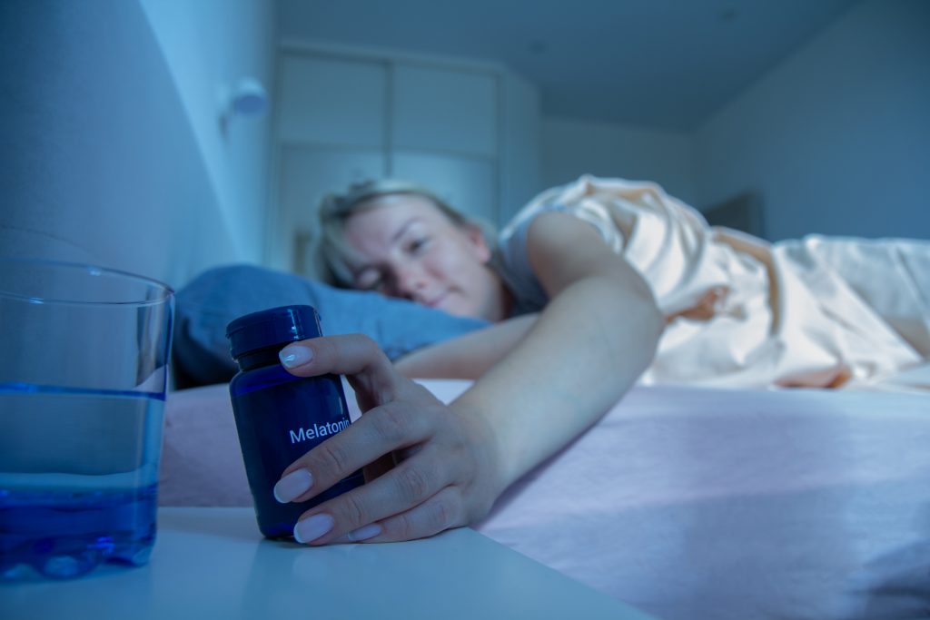 Woman reaching for melatonin bottle during bedtime