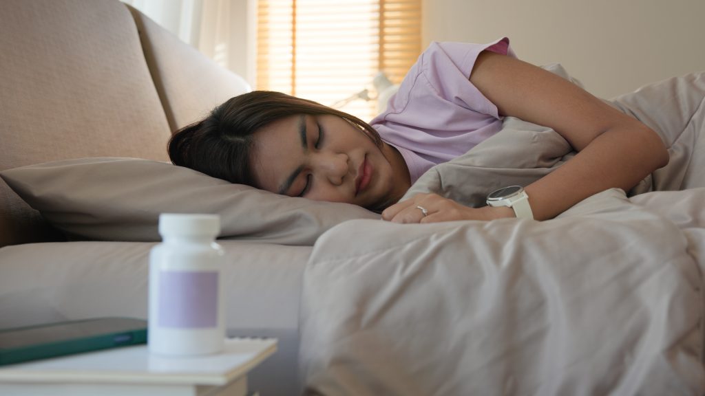 Young adult woman black asia people take herbal CBD pill bottle lying down on soft cozy bed deep sleep aid calm. Waking up happy serene relax drug anti aging good health care fall asleep till morning.