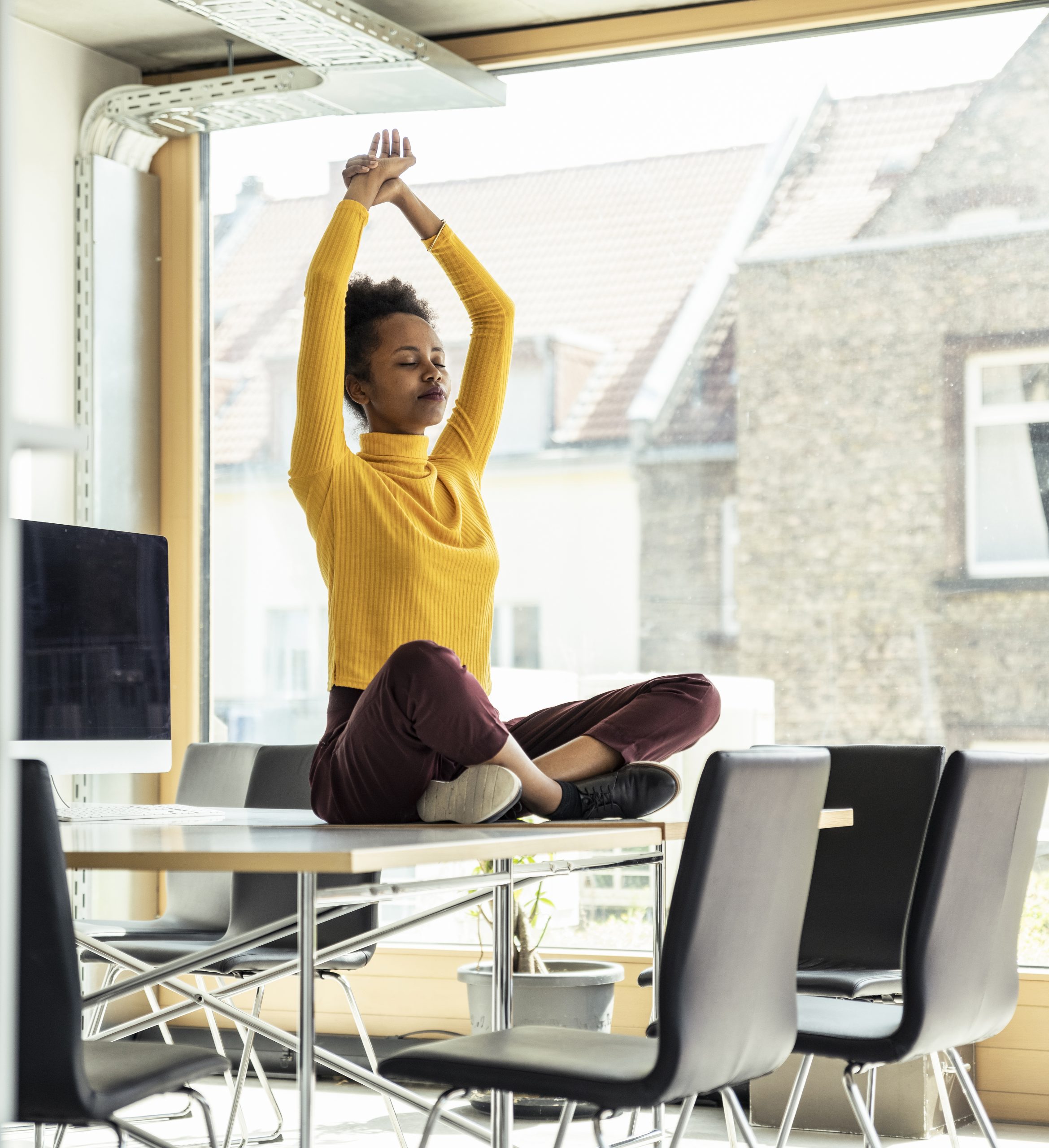 Female professional with arms raised meditating on desk at office
